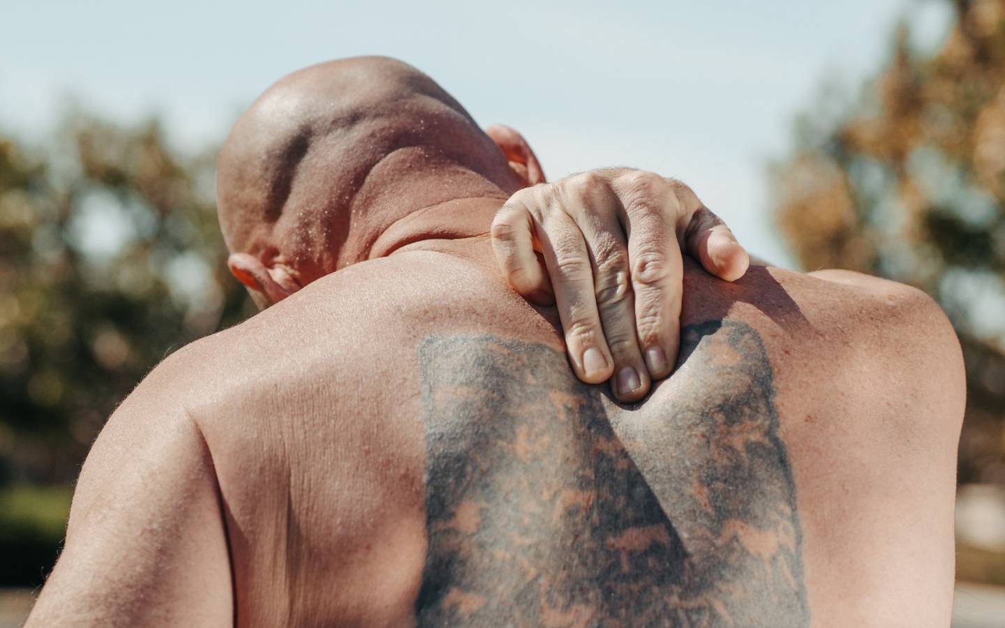 Hombre dandole la espalda a la cámara y mostrando su tatuaje, se toca parte alta de la espalda.