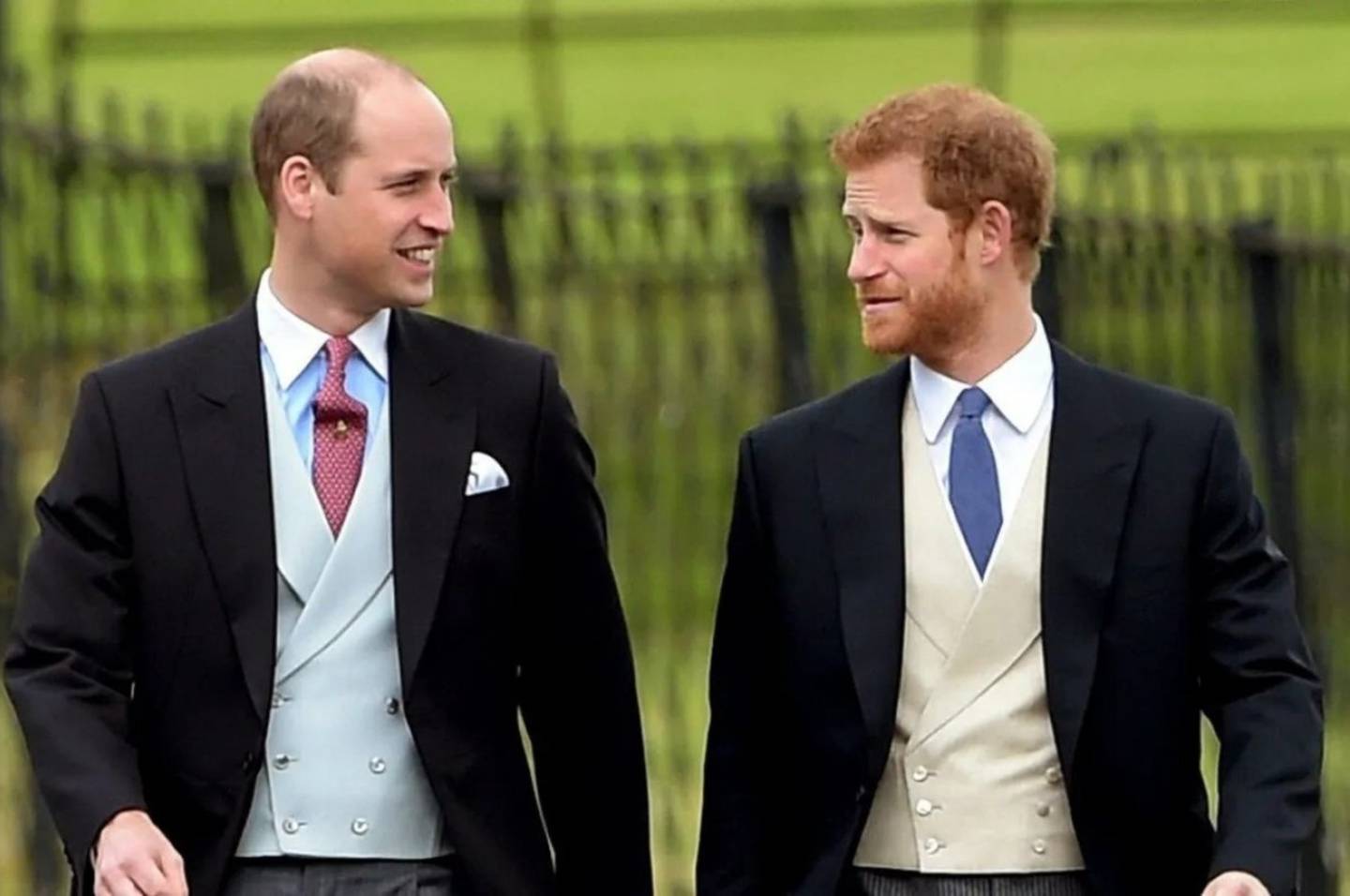 Príncipes William y Harry de la monarquía británica se miran a la cara con expresión sonriente.
