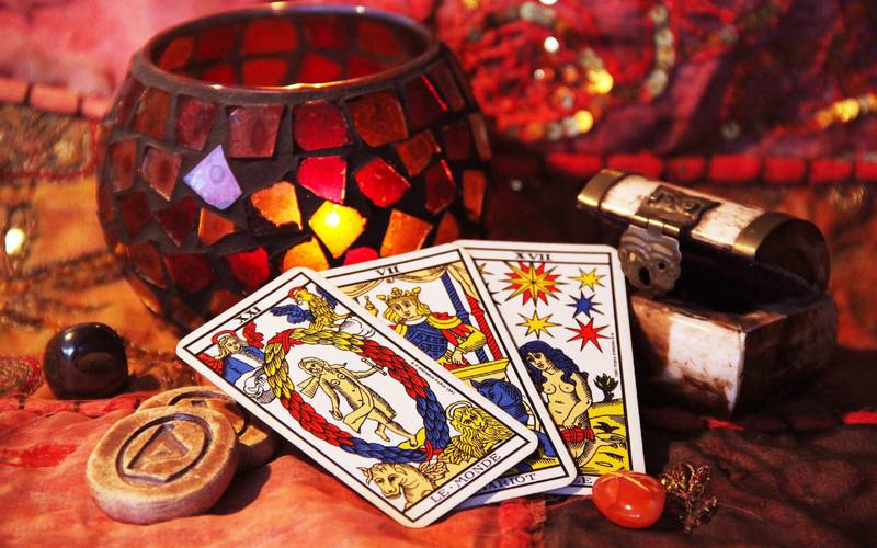 Tres cartas del tarot aparecen apoyadas junto a una vela y otros elementos mágicos como gemas y runas.