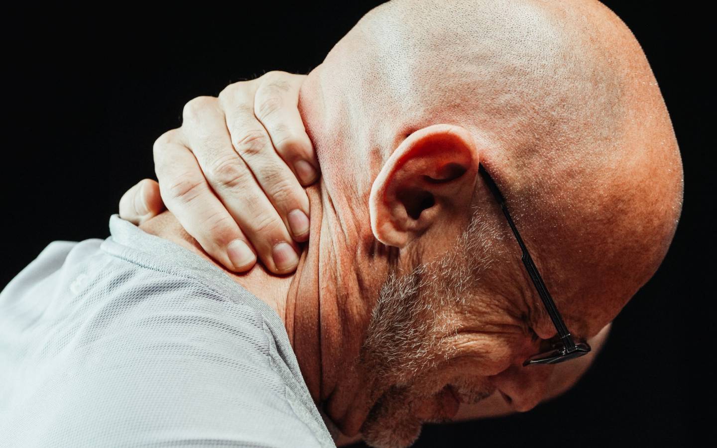 Un hombre de mediana edad, calvo y con lentes, toca su cuello en una expresión de dolor.