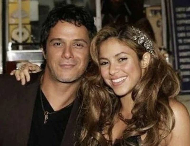 Imagen de medio plano de Shakira y Alejandro Sanz abrazados de lado. Alejandro Sanz viste ua chaqueta café y una polera negra.Shakira lleva un top negro de tirantes, y una diadema en la cabeza.