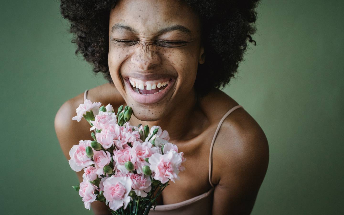 Una mujer joven sostiene un ramo de flores rosas y una ámplia sonrisa en el rostro.