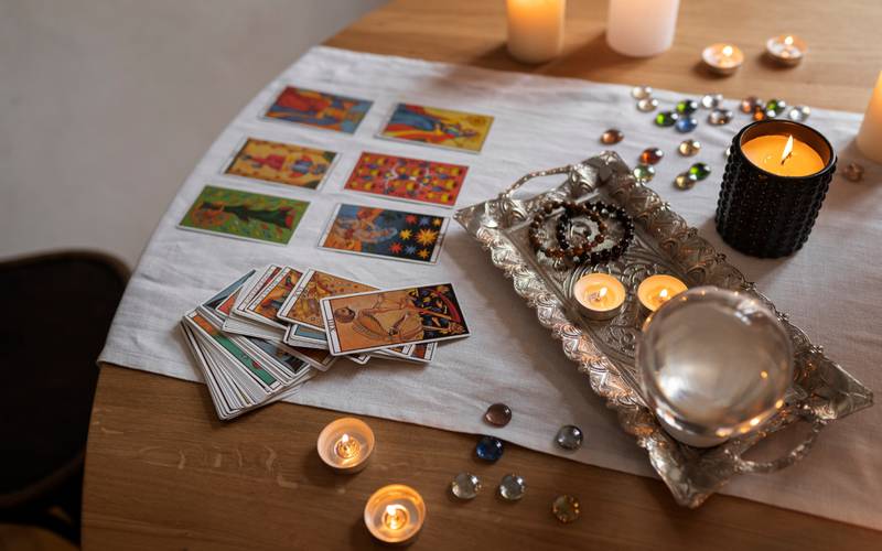 Cartas de Tarot desplegadas sobre una mesa en una lectura. Las acompañan velas y un mantel blanco.