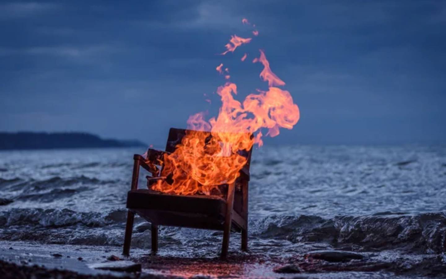Una silla se quema en la orilla del mar en un momento que parece el amanecer o el ocaso.
