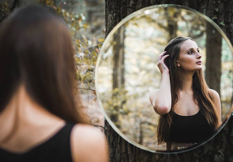 Mujer viéndose al espejo en un bosque. El reflejo del espejo mira hacia otro lado.