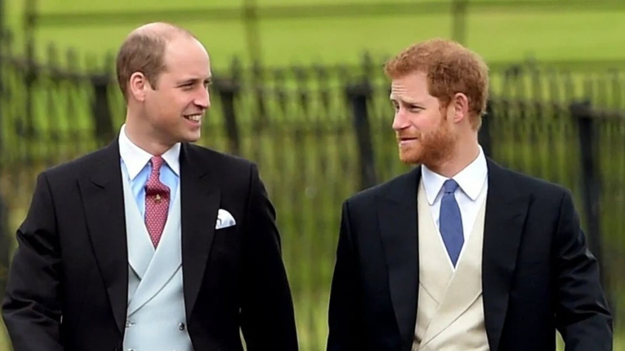 Príncipes William y Harry de la monarquía británica se miran a la cara con expresión sonriente.