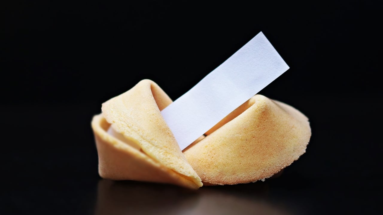 Una galeta de la suerte con un mensaje en blanco saliendo de ella, sobre un fondo negro.