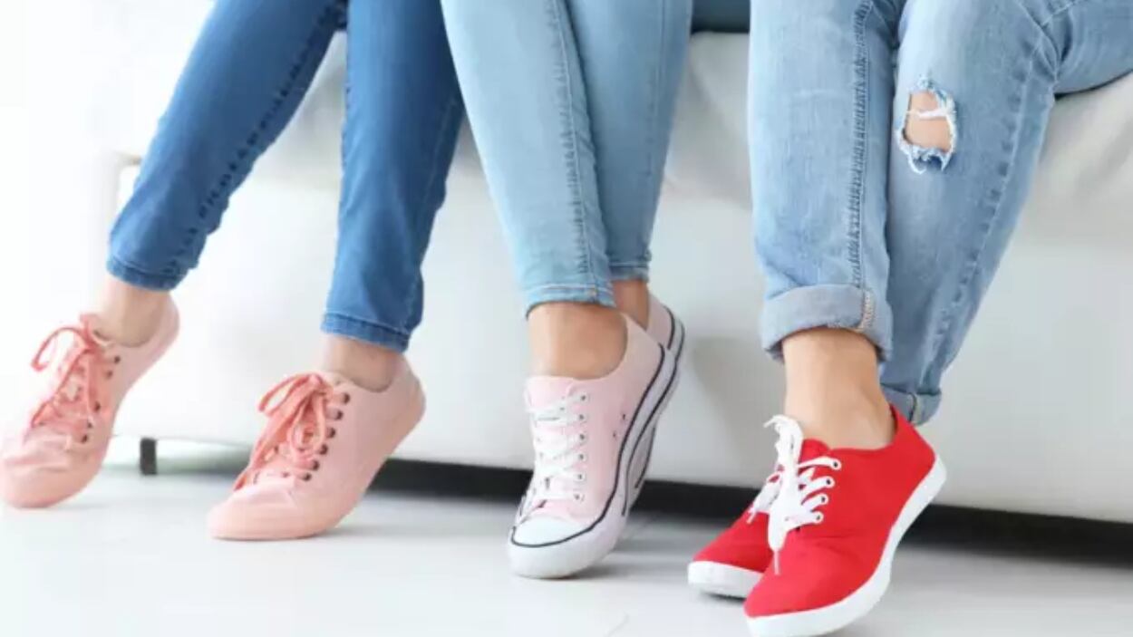Piernas de tres personas sentadas en un sillón en posturas diferentes. Las tres llevan jeans y tenis de colores.