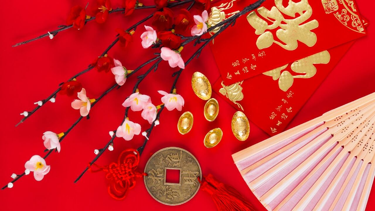 Fondo rojo sobre el que descanzan unas ramas de cerezos en flor y algunos elementos decorativos orientales para atraer fortuna.