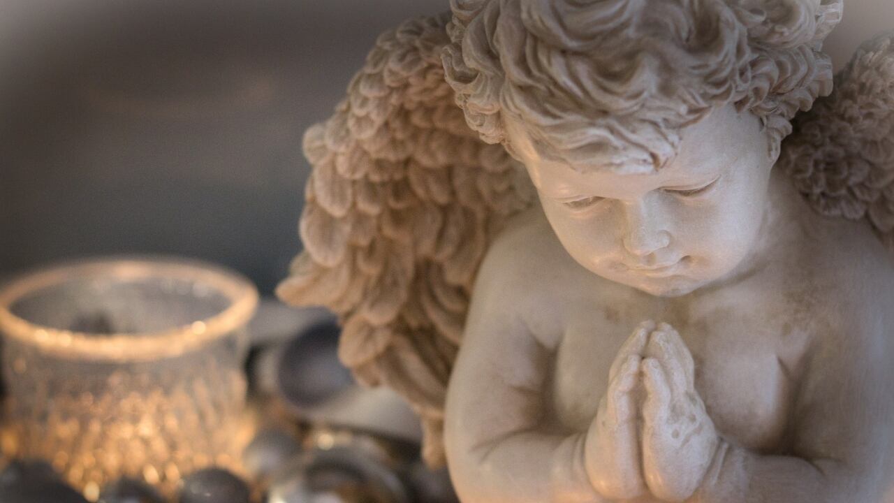 Figurín de cerámica o yeso de un ángel de aspecto infantil, acompañado de una vela encendida.