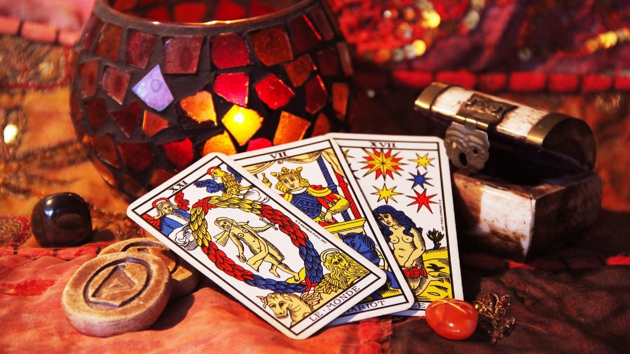 Tres cartas del tarot aparecen apoyadas junto a una vela y otros elementos mágicos como gemas y runas.