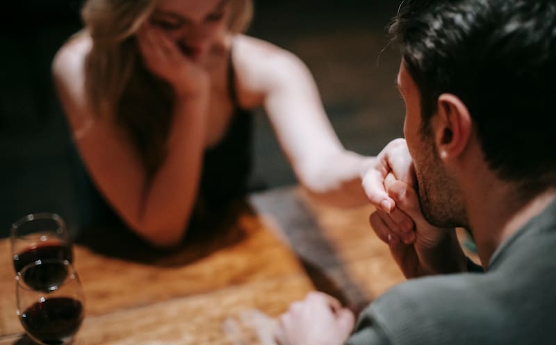 Una pareja está sentada frente a frente en una mesa de un restauran. Él le toma seductoramente la mano.